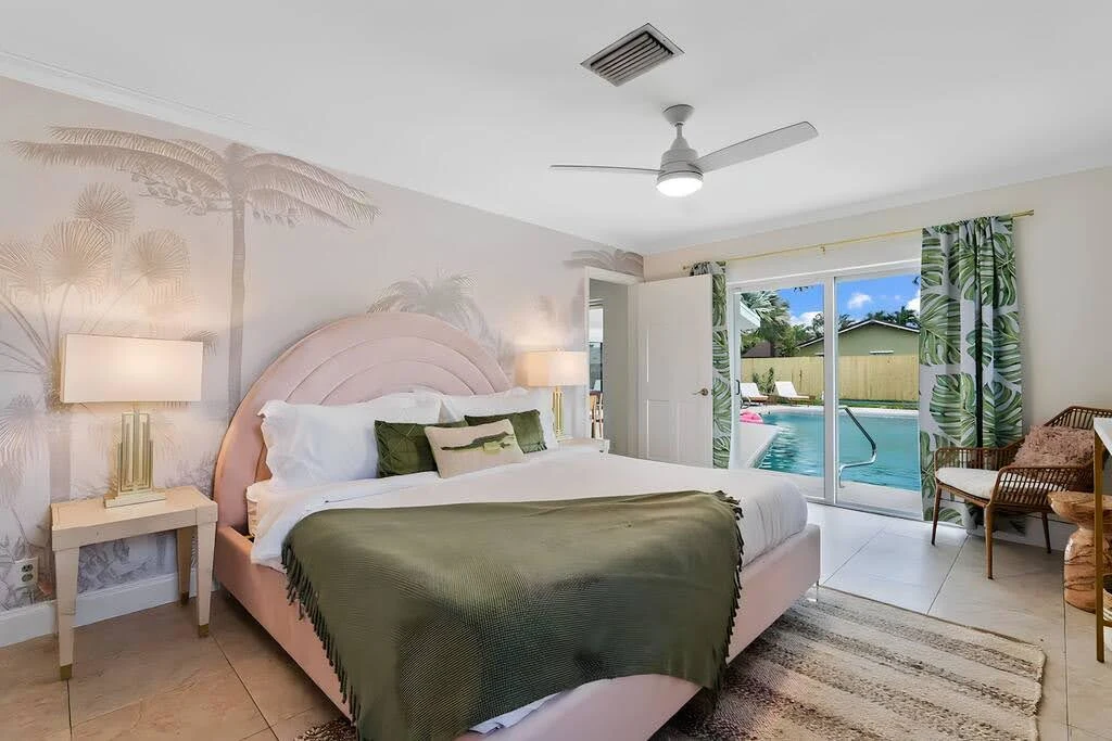 Airbnb bedroom with blush walls, pale wood furniture, and tropical greenery outside