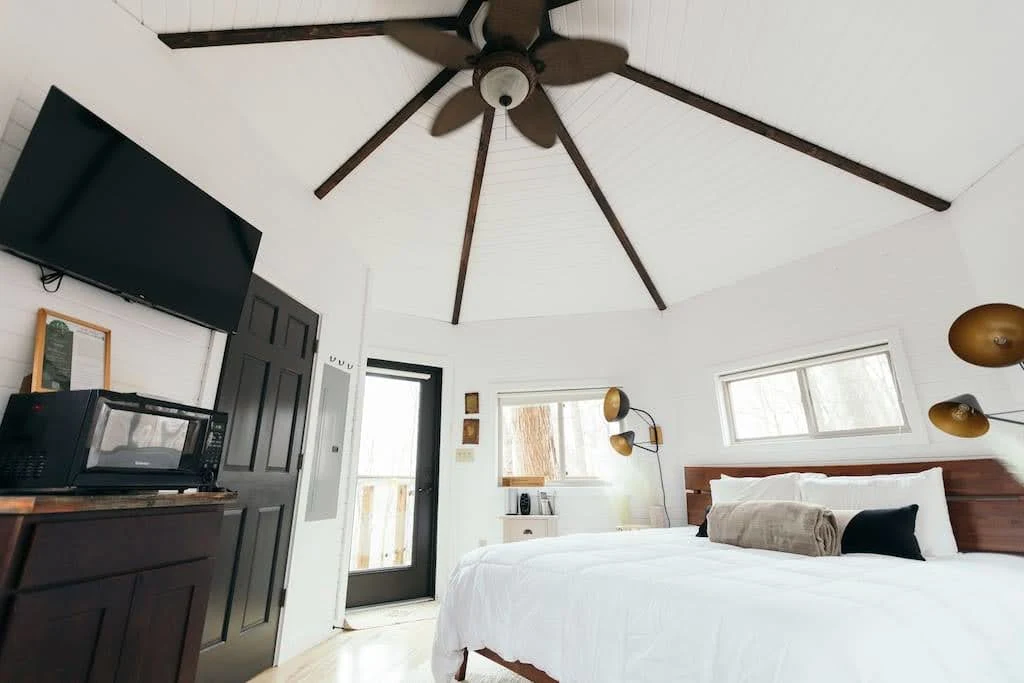 Industrial Airbnb bedroom with a black feature wall, white bed, and large ceiling fan