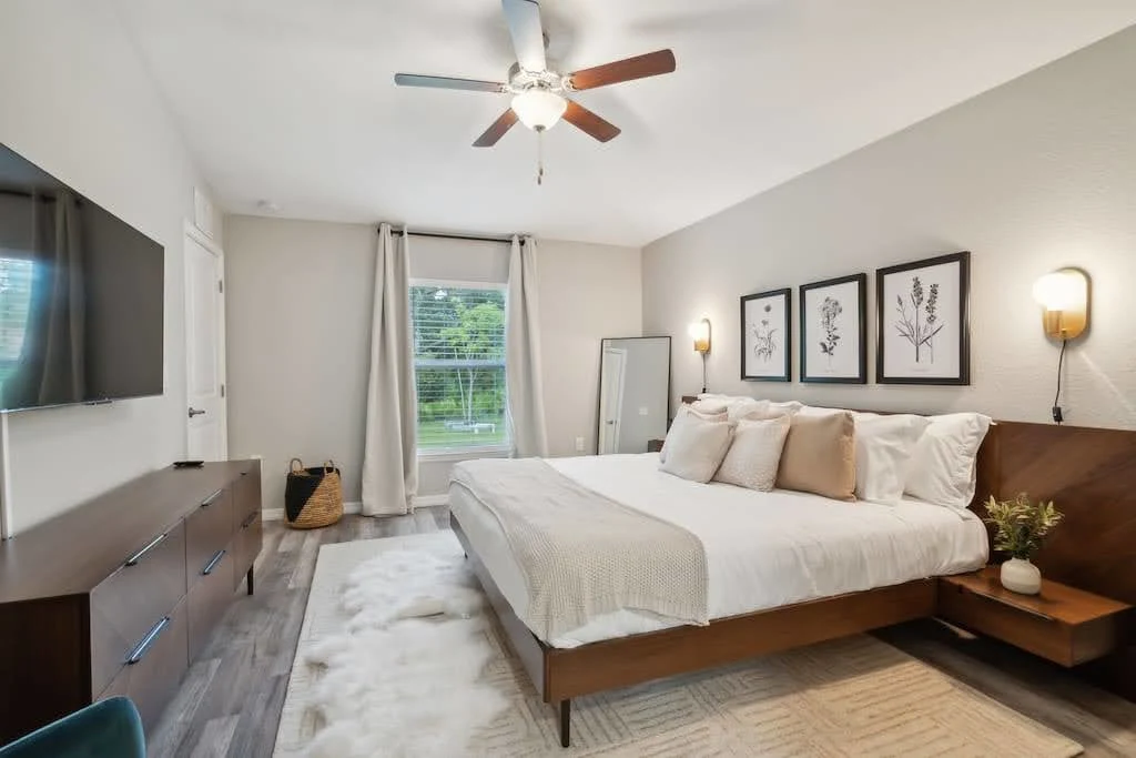 Neutral Airbnb bedroom with a cream bed, wood furniture, and framed botanical art