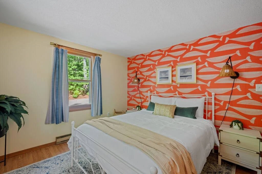 Airbnb bedroom with an orange abstract accent wall and a simple gray bed