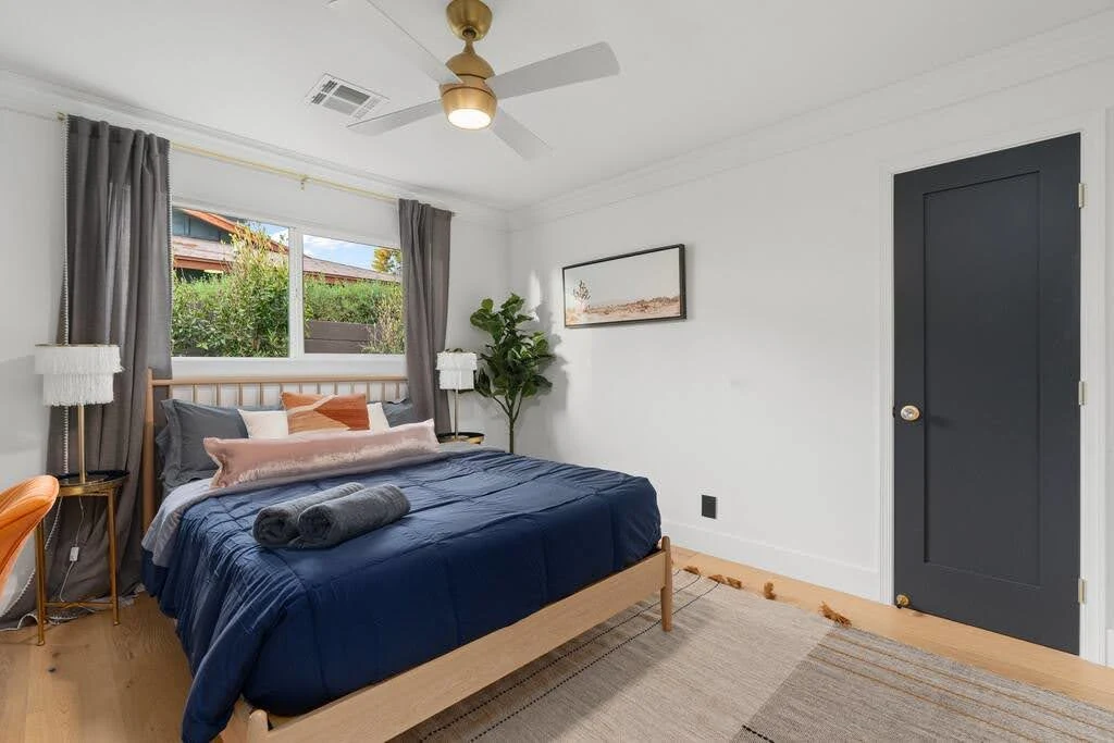 Airbnb bedroom with navy bedding, dark doors, white walls, and warm wood furniture