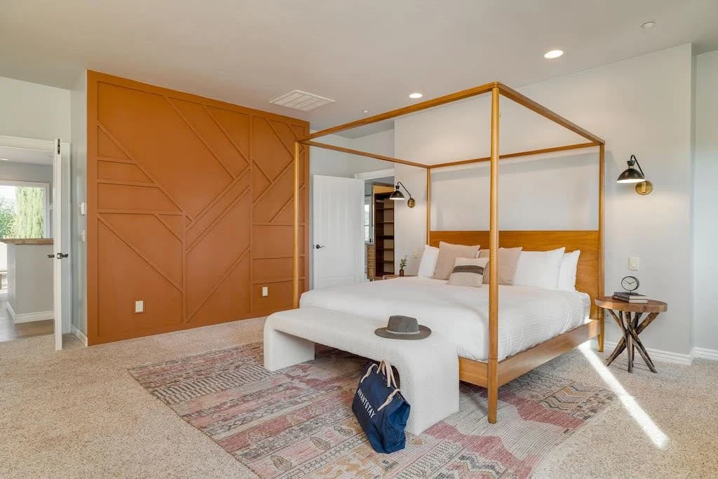 Contemporary Airbnb bedroom with a slim wood canopy bed and rust-colored wall