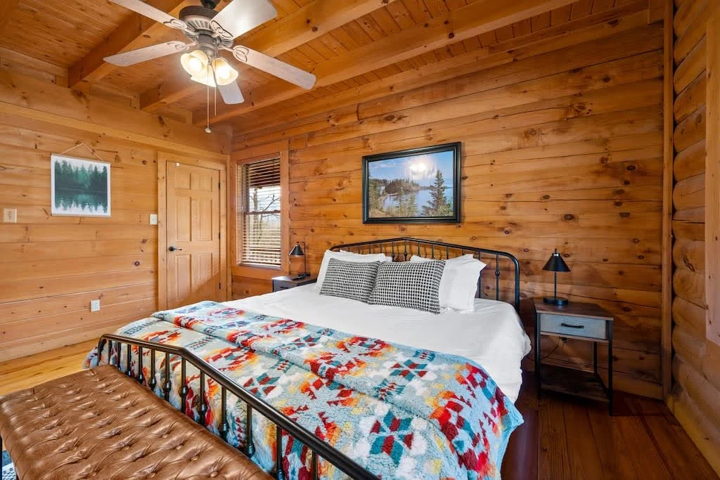Wood-paneled cabin bedroom with a colorful quilt and compact furniture